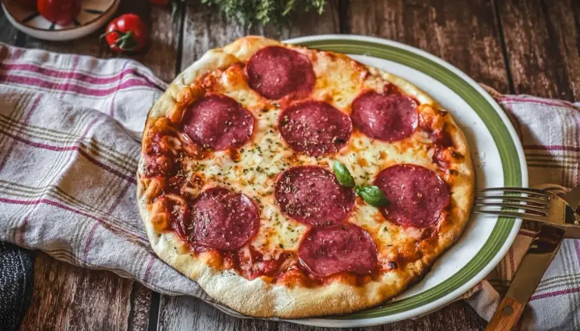 Eine köstliche Pizza Salami mit geschmolzenem Käse und frischem Basilikum auf einem Holztisch.