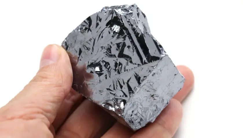 Ein Mensch hält ein Stück Silizium, dessen Oberfläche wie eine glänzende, metallische Haut mit komplexen Mustern aussieht.