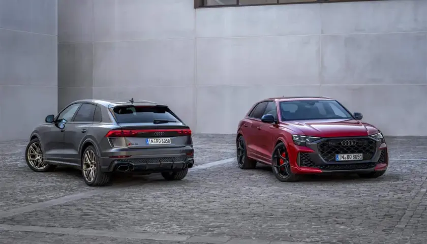 Due Audi RS Q8, una grigia e una rossa, parcheggiate su un selciato di fronte a un edificio moderno.