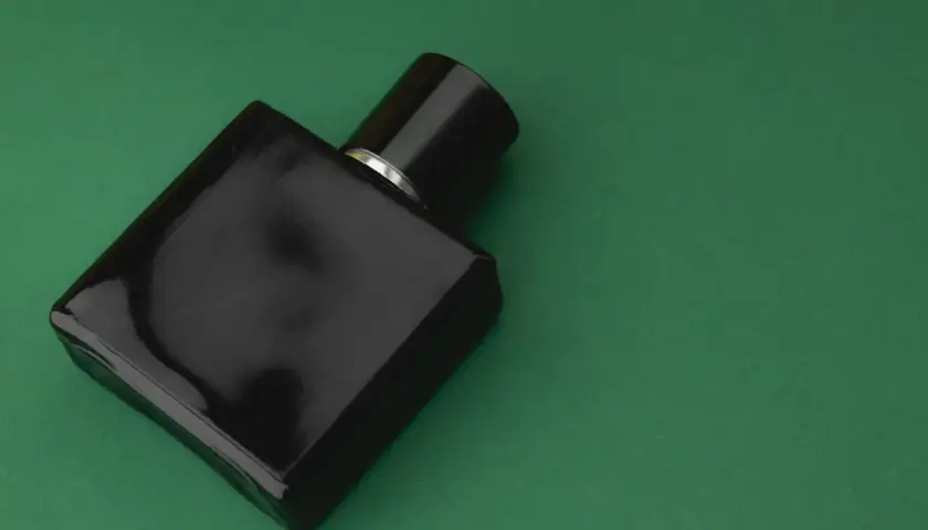 Czarna butelka perfum z nutami **vetiver** na zielonym tle.