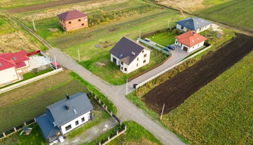 Widok z lotu ptaka na kilka domów jednorodzinnych na tle pól i zieleni.