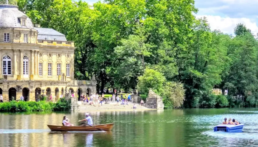 Ein sonniger Tag am Monrepos Schloss. Menschen genießen Bootsfahrten auf dem See vor dem barocken Gebäude, umgeben von üppigem Grün.