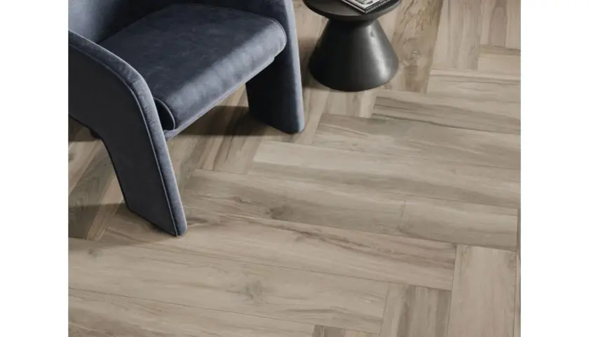 Un fauteuil moderne repose sur un sol en pose carrelage imitation parquet en chevrons, créant une ambiance chaleureuse et élégante.