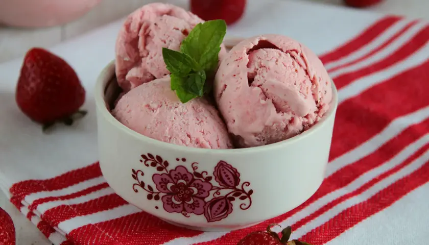 Pyszne lody truskawkowe w miseczce, ozdobione miętą. Idealne na lato, pokazują, jak zrobić lody truskawkowe.