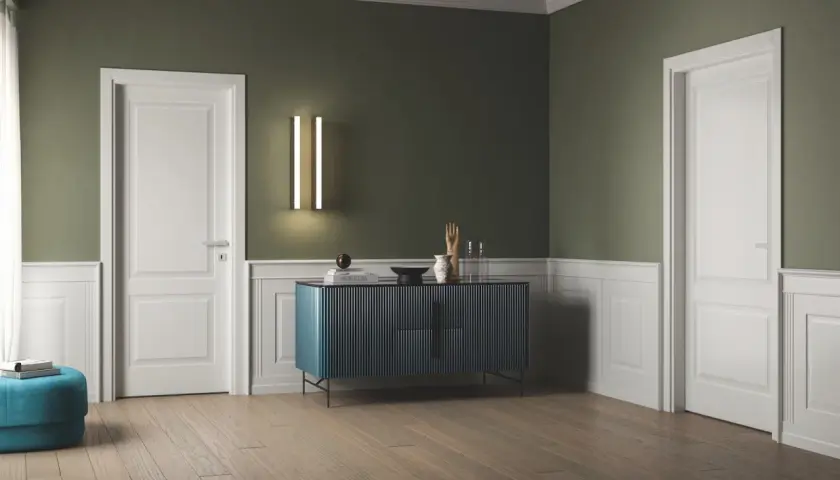 Interno con pareti verde salvia e boiserie bianca, porte bianche, un mobile blu e un pouf turchese.