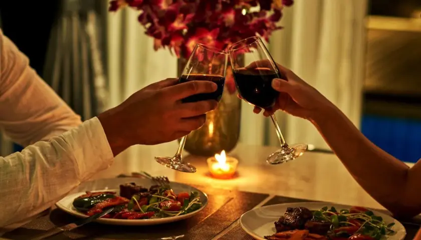 Romantyczna kolacja dla dwojga przy świecach. Dwie pary kieliszków z czerwonym winem unoszą się w geście toastu.