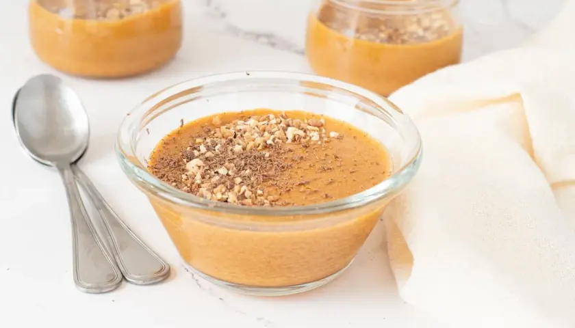 Delicioso postre cremoso, como baba de camelo, servido en un cuenco de cristal y espolvoreado con frutos secos y virutas de chocolate.
