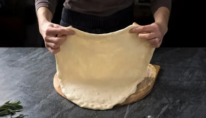 Ręce rozciągają elastyczne ciasto na pizzę, idealne do szybkiego przepisu na ciasto do pizzy.