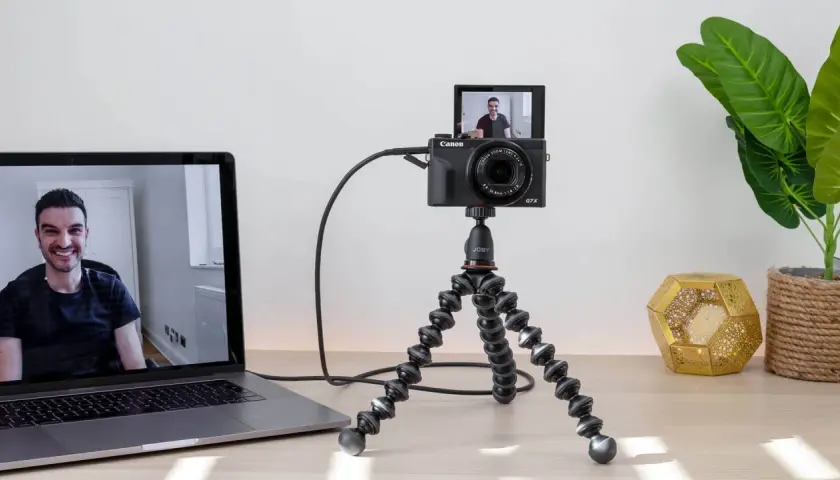 Configuración para usar webcam como cámara de seguridad: una Canon G7X en un trípode flexible, conectada a un portátil que muestra a un hombre sonriendo.