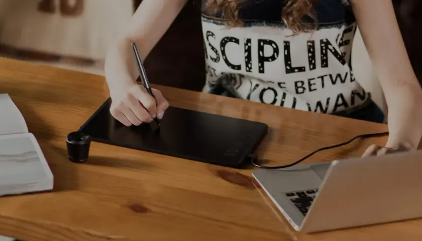 Osoba rysuje na tablecie graficznym, który służy do cyfrowego tworzenia grafiki i ilustracji, podłączonym do laptopa.