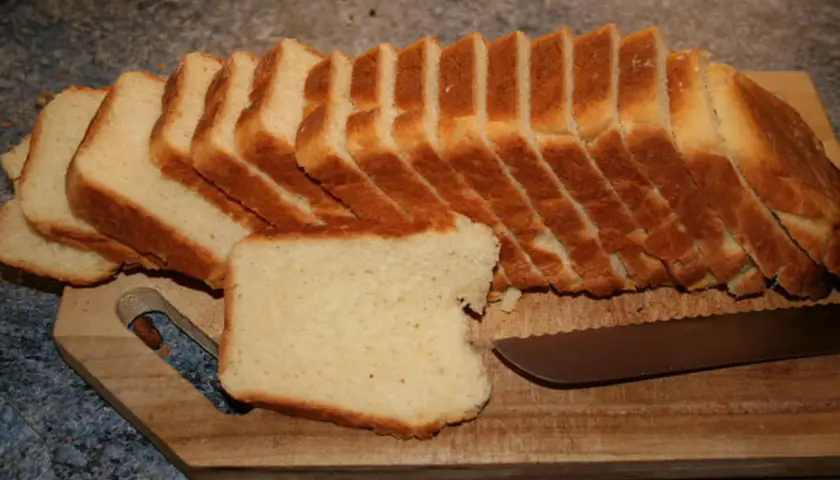 Tranches de pâte à pain de mie dorées et moelleuses, prêtes à être dégustées sur une planche en bois avec un couteau.
