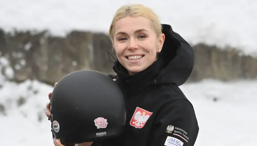 Uśmiechnięta Klaudia Adamek trzyma kask. Na jej kurtce widnieje godło Polski.