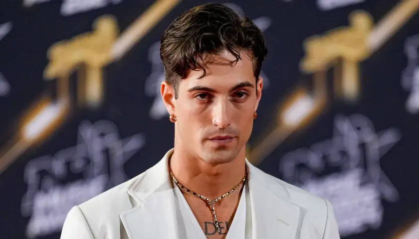 Damiano David w białej marynarce, z naszyjnikiem i kolczykami, gotowy na koncert.