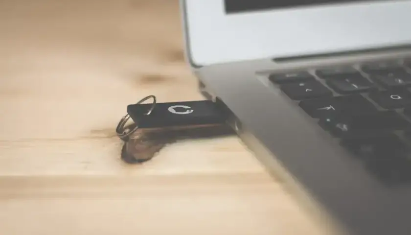 Czarny, bootowalny pendrive z logo podłączony do laptopa na drewnianym biurku.