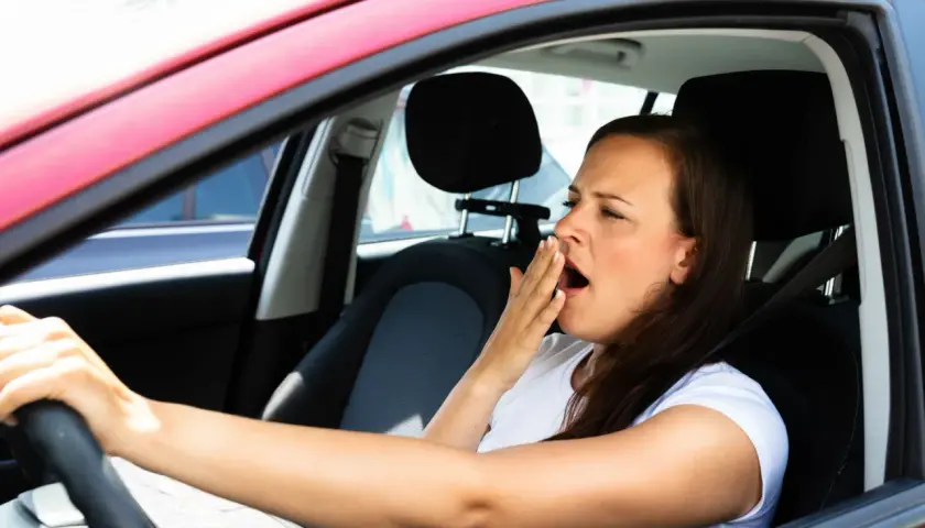 Mujer bosteza al volante, un claro ejemplo de qué puede causar somnolencia en un conductor.