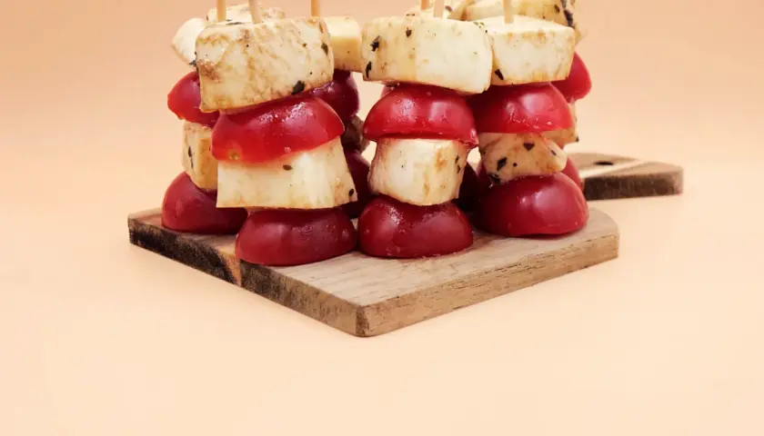 Koreczki z mozzarellą i pomidorkami koktajlowymi, przyprawione ziołami, ułożone na drewnianej desce.