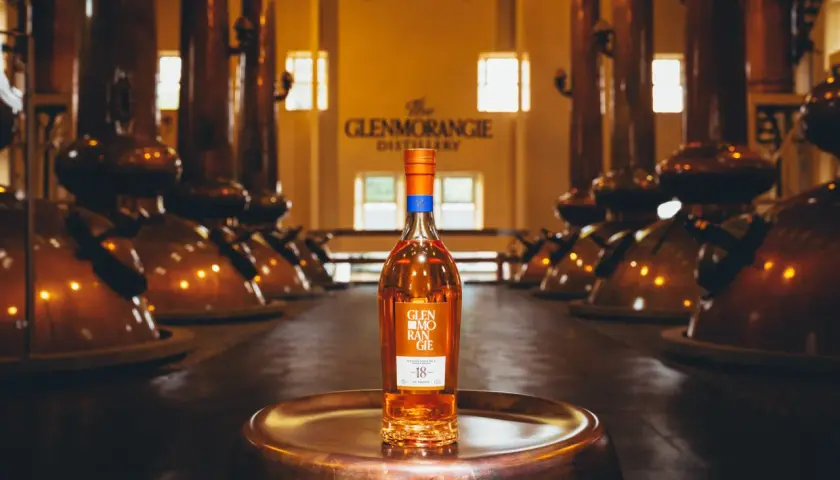 Bouteille de whisky Glenmorangie 18 ans posée sur un plateau en cuivre, au cœur de la distillerie Glenmorangie, entourée d'alambics en cuivre.
