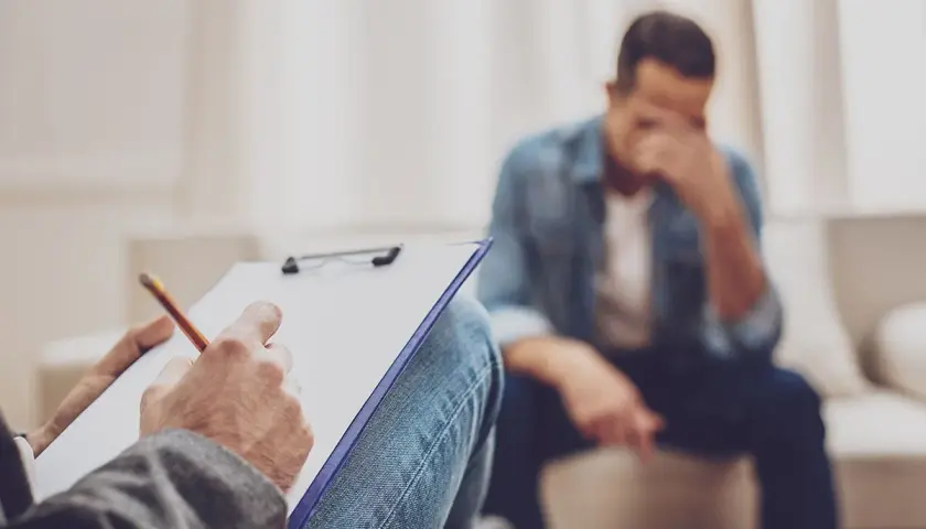 Rozmowa z terapeutą o trudnym rozwodzie z osobą chorą psychicznie. Mężczyzna w rozpaczy, terapeuta notuje.