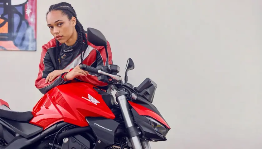 Joven con chaqueta de cuero posa junto a una moto roja Honda Hornet. Lista para el rodaje moto 125.