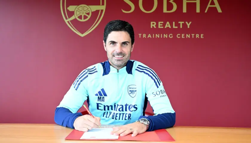 Mikel Arteta, trener Arsenalu, podpisuje dokumenty. Uśmiecha się do aparatu, ubrany w klubowy dres.