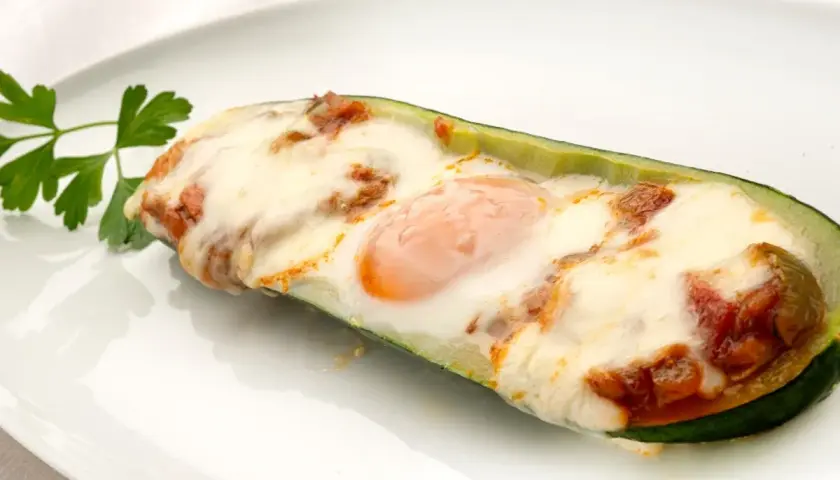 Deliciosos calabacines rellenos con huevo y queso gratinado, adornados con perejil fresco.
