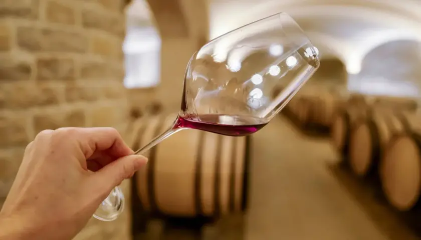 Verre de vin rouge tenu dans une cave à vin de Dijon, avec des tonneaux en arrière-plan. Une dégustation de vin inoubliable.