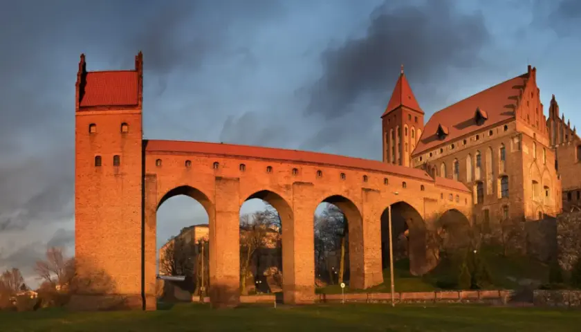 Imponujące zamki na Pomorzu, z cegły i czerwonym dachem, oświetlone zachodzącym słońcem, na tle burzowego nieba.