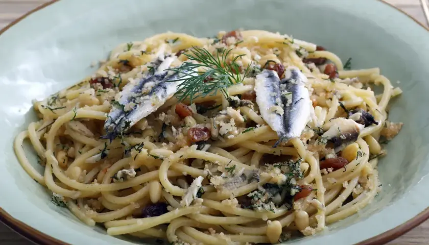 Un plat de pâtes aux sardines, garni de pignons de pin, de raisins secs et d'aneth frais.