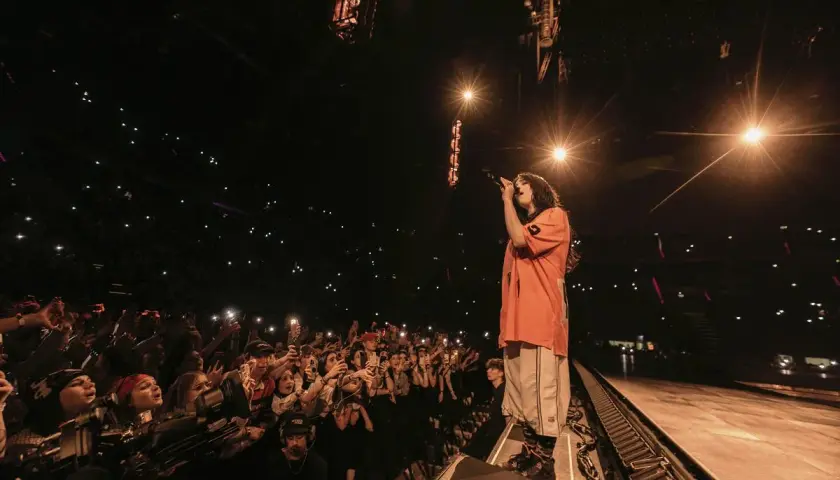 Billie Eilish w Polsce śpiewa dla tłumu fanów, którzy oświetlają scenę telefonami.