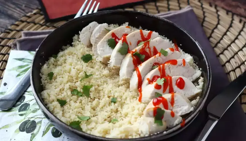 Delizioso pollo in padella a fette, servito su un letto di couscous e guarnito con prezzemolo e salsa piccante.