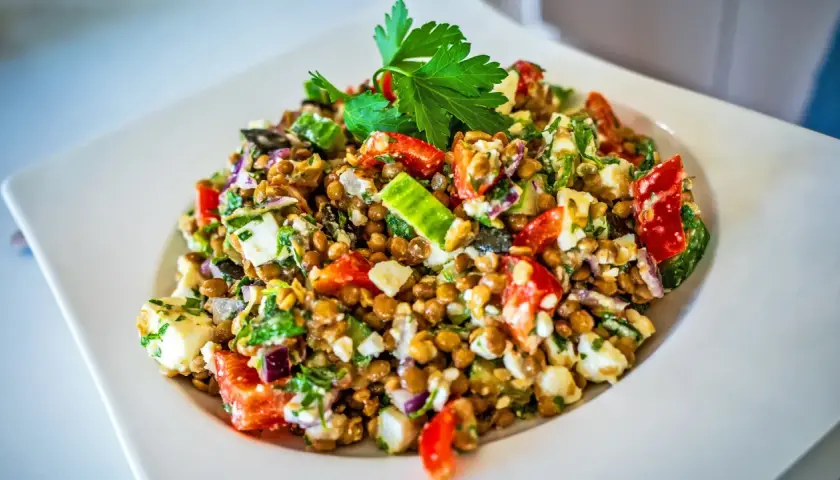 Ein bunter Linsensalat mit Feta, Tomaten, Gurken und frischer Petersilie, garniert mit einem Petersilienblatt.