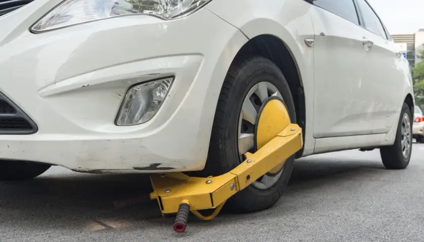 Ruota anteriore di un'auto bianca bloccata da un dispositivo giallo, segno di confisca veicolo.