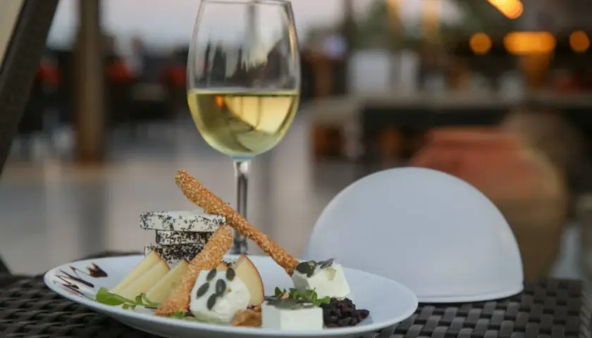 Un verre de vin blanc et une assiette de fromages variés, parfaits pour savoir que manger avec un gewurztraminer.