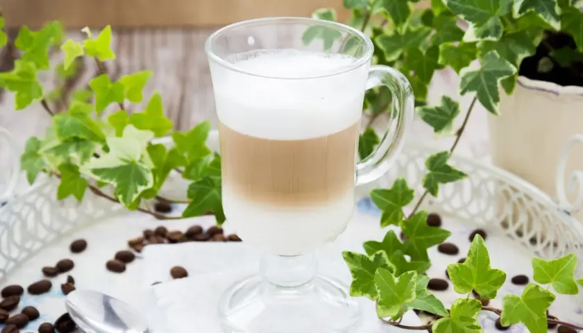 Warstwowe latte w szklance, otoczone bluszczem i ziarnami kawy. Prosty sposób, jak zrobić latte bez ekspresu.