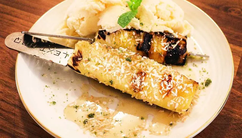 Grillad ananas på spett, toppad med kokosflingor, serveras med vaniljglass och en myntakvist. En härlig dessert!