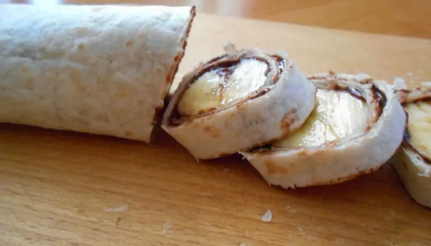 Roladki z tortilli z bananem i czekoladą na desce.