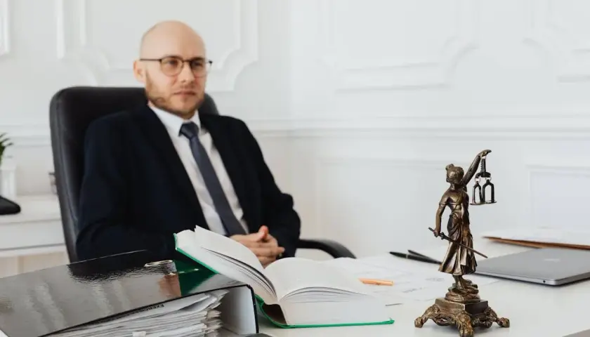 Prawnik w garniturze siedzi przy biurku, obok niego stos dokumentów i otwarta księga. Zastanawiasz się, ile kosztuje notariusz?