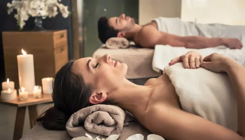 Para relaksu w spa: para leży na stołach do masażu, otoczona świecami i kwiatami. To idealne miejsce, by zapomnieć o codzienności.