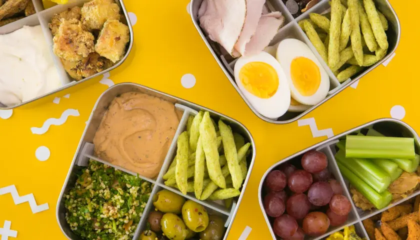 Four bento boxes filled with colorful, healthy foods, perfect for bento for beginners. Includes chicken, eggs, olives, grapes, and more.