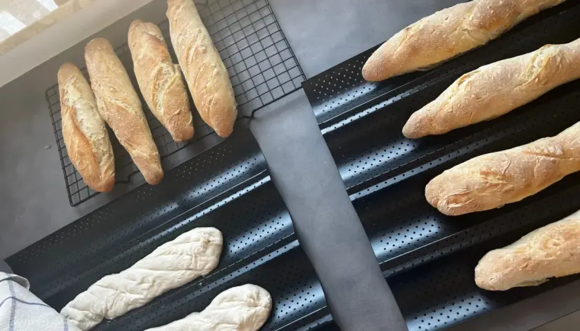 Gotowe do pieczenia bagietki po francusku, świeżo wyrośnięte ciasto i wypieczone bochenki na ruszcie.
