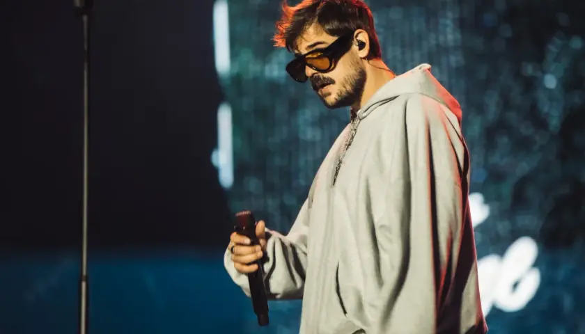 Taco Hemingway w okularach i szarej bluzie z kapturem, trzymający mikrofon. Fani czekają na koncert Taco Hemingway 2026.