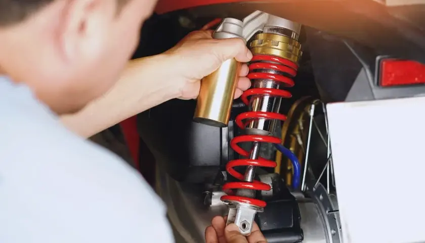 Mechanik wymienia czerwoną sprężynę amortyzatora w motocyklu.