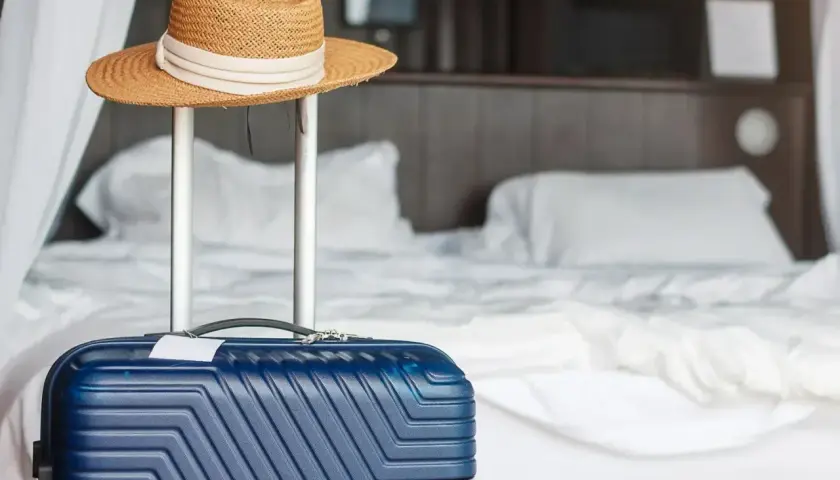 Błękitna walizka i słomkowy kapelusz gotowe do wyjazdu. Zastanawiasz się, co można zabrać z hotelu? Pamiętaj o swoich rzeczach!