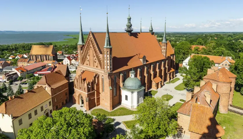 Zamek Frombork z lotu ptaka, z dominującą bazyliką katedralną i wieżami obronnymi, nad błękitną wodą Zalewu Wiślanego.