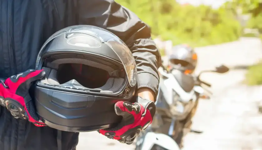 Motocyklista w czerwono-czarnych rękawicach trzyma kask. Warto wiedzieć, co to jest pinlock w kasku, by uniknąć parowania wizjera podczas jazdy.