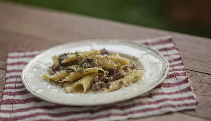 Pasta con ragú bianco, un plato reconfortante con carne picada y hierbas frescas, servido en un plato blanco sobre una servilleta a rayas.