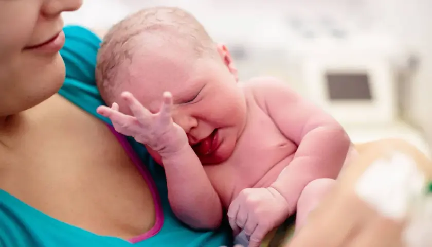 Neugeborenes Baby wird von der Mutter gehalten. Die Nabelschnur wird auspulsieren gelassen, um dem Kind alle wichtigen Nährstoffe zu übergeben.