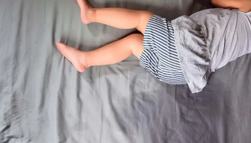 Gambe di bambino su lenzuola grigie. Un piccolo incidente notturno, forse legato all'enuresi notturna, ha lasciato un segno.