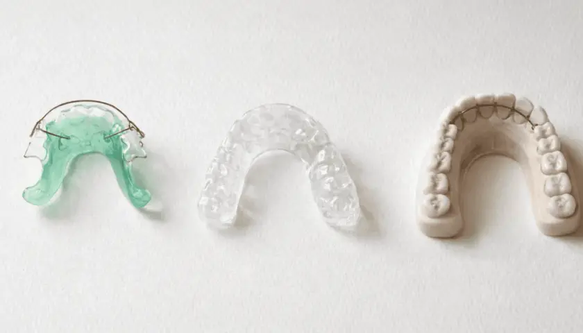 Tres dispositivos dentales: un retenedor verde, un retenedor transparente y un modelo de dientes con barra retenedora.