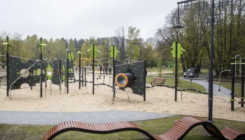 Nowoczesny plac zabaw w parku na zdrowiu z piaskownicą, ściankami wspinaczkowymi i nietypową ławką.